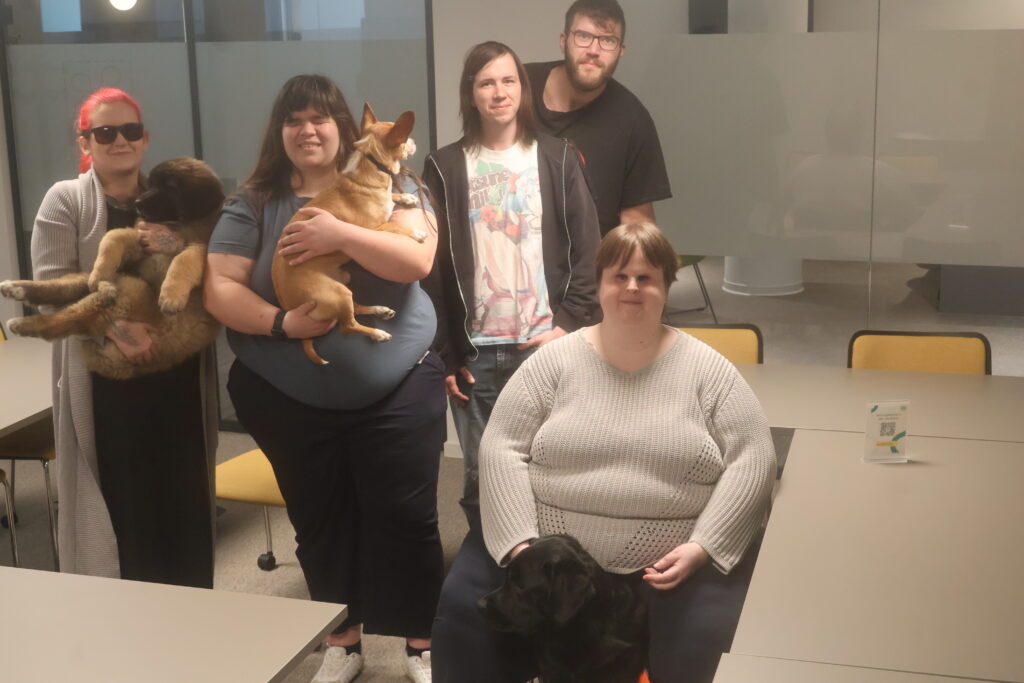 Gruppenfoto des inklusivio-Teams. Vorne rechts Nathalie mit Odin sitzend, dahinter von links nach rechts Angelina mit Anouk, Tanja mit Timon, und Max. Seitlich hinter Max steht Chris